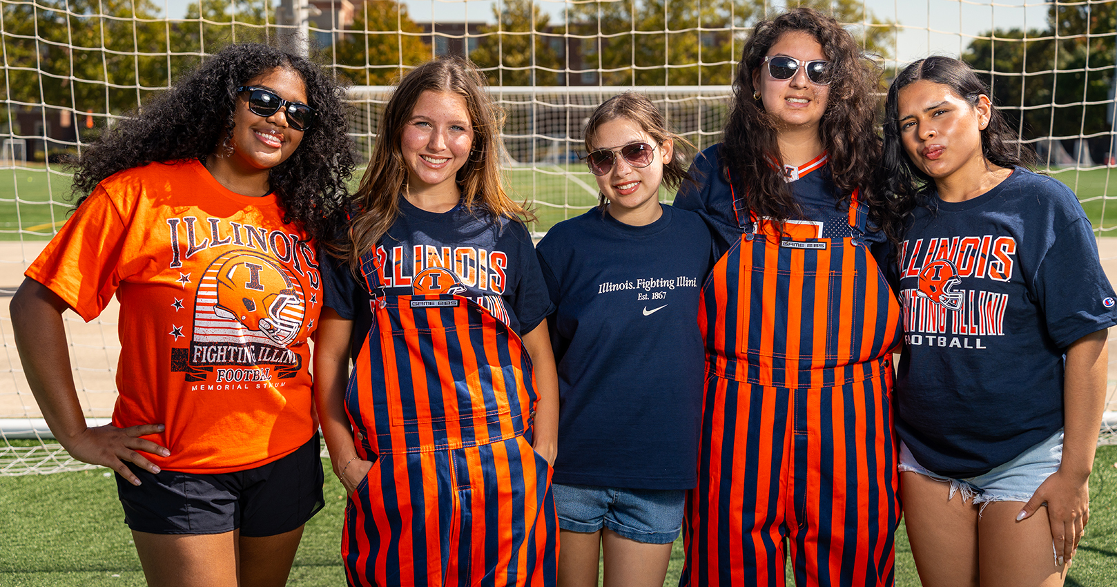 picture of 5 students Wearing Illini gear standing on a soccer field